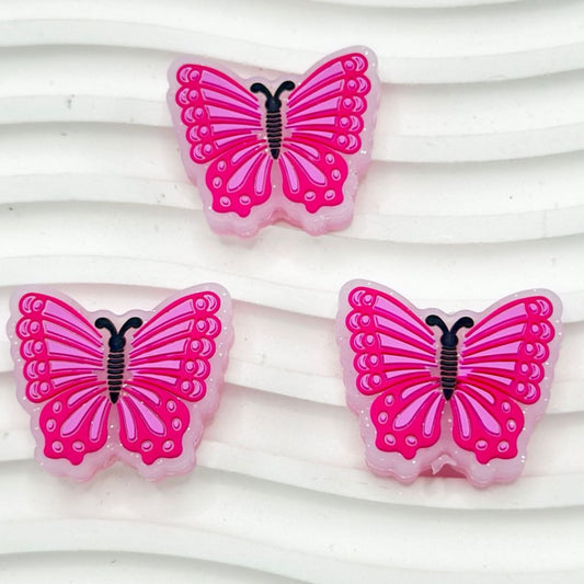 A set of silicone beads in the shape of butterflies, with the dominant color being pink and they have glitter on them.

