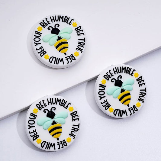 Three round silicone beads with a bee design and the text 'BEE HUMBLE, BEE TRUE, BEE WILD, BEE YOU' printed on them.

