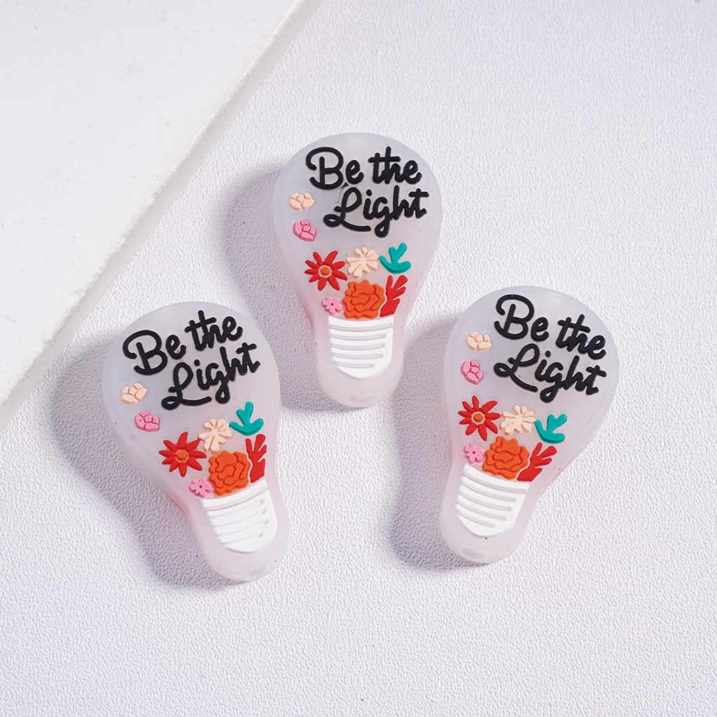 Three light bulb-shaped cutters with 'Be the Light' text and floral designs on a white background