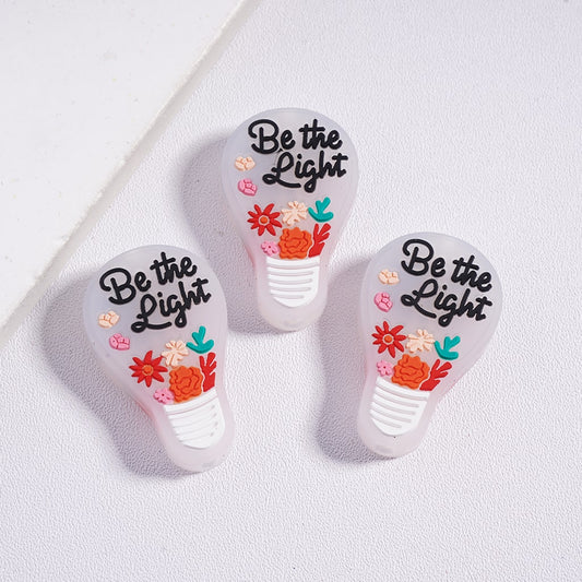 Three light bulb-shaped cutters with 'Be the Light' text and floral designs on a white background