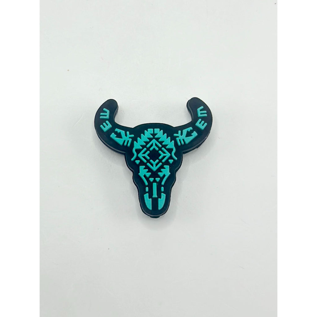A silicone bead in the shape of a cow or bull head with teal geometric patterns.

