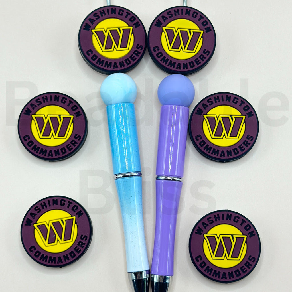 Two pens, one blue and one purple, with matching round stickers featuring a logo and text on a white background.

