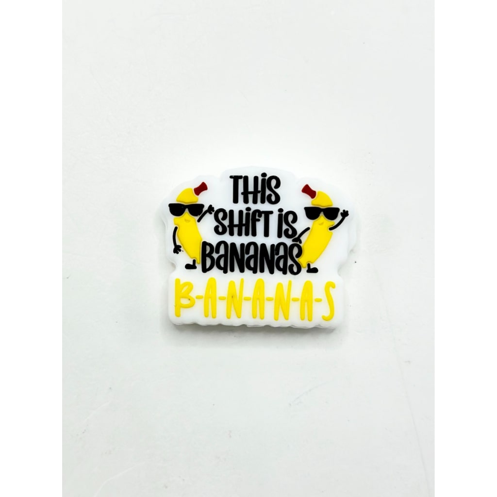 A silicone focal bead with the phrase 'This Shift is Bananas' printed on it, predominantly yellow with black text and graphic elements.

