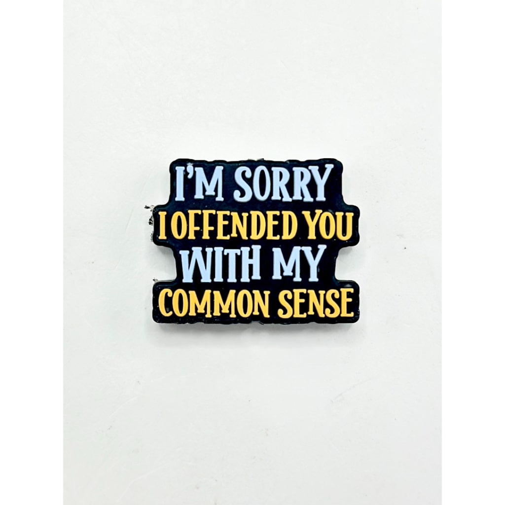 A silicone bead with the text 'I'M SORRY I OFFENDED YOU WITH MY COMMON SENSE' printed on it, primarily in black color with white and yellow text.

