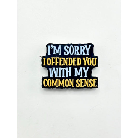 A silicone bead with the text 'I'M SORRY I OFFENDED YOU WITH MY COMMON SENSE' printed on it, primarily in black color with white and yellow text.

