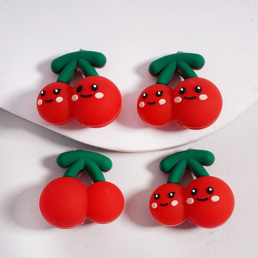 Two pairs of red cherry-shaped earrings with smiling faces on a white plate.

