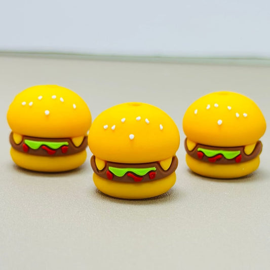 A set of silicone beads shaped like hamburgers with yellow buns, red tomato slices, green lettuce, and brown meat.

