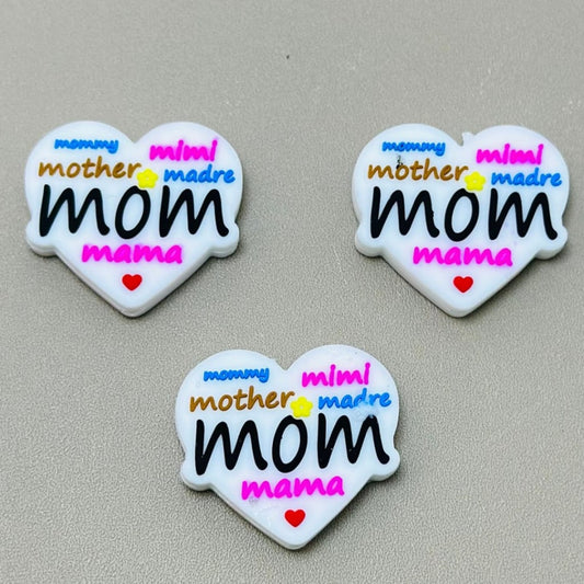 Heart-shaped silicone beads with the word 'mom' and variations like 'mother', 'mama', and 'mummy' written on them in different colors.

