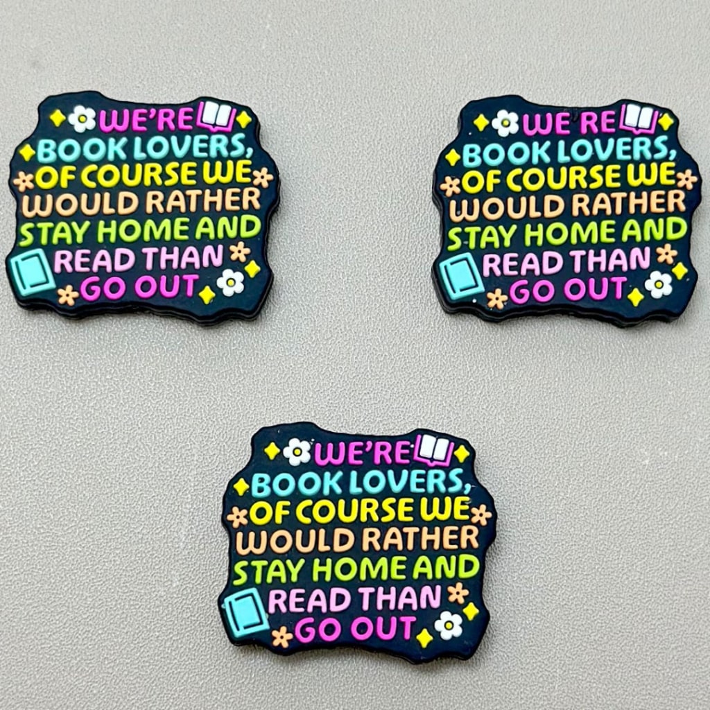 A set of three silicone focal beads with the phrase 'We would rather stay home and read than go out' printed on them, in various colors.

