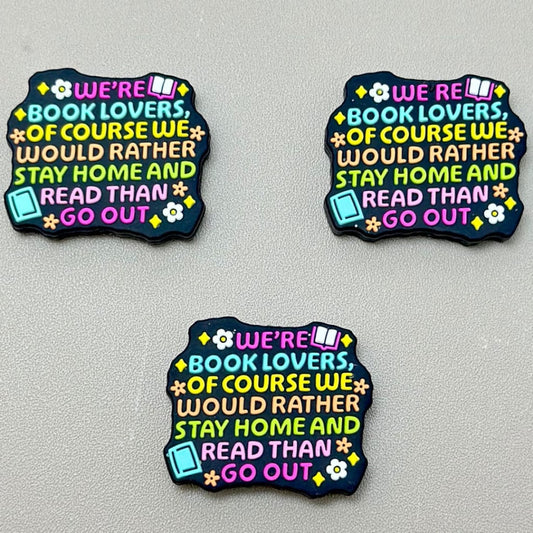 A set of three silicone focal beads with the phrase 'We would rather stay home and read than go out' printed on them, in various colors.

