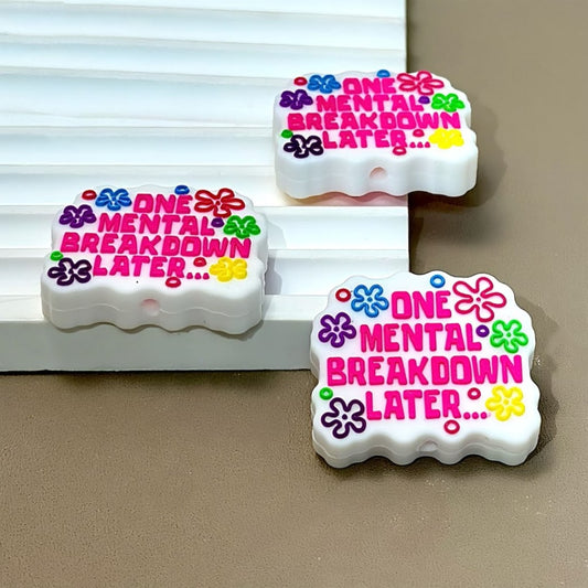 Silicone beads with the phrase 'One Mental Breakdown Later...' printed on them, adorned with colorful floral designs.


