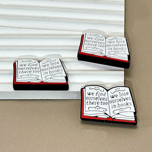A set of silicone beads designed to look like open books with the words 'we find ourselves there too - we lose ourselves in books' printed on them.

