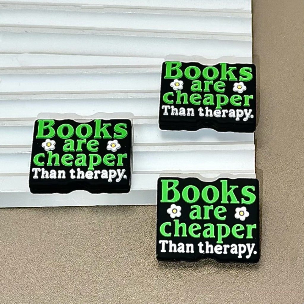 Rectangular silicone beads with the text 'Books are cheaper Than therapy' printed on them, displayed against a light background.

