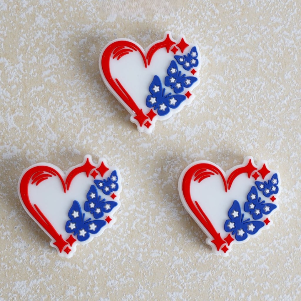 Three heart-shaped cookies with red, white, and blue butterfly designs on a textured beige background.


