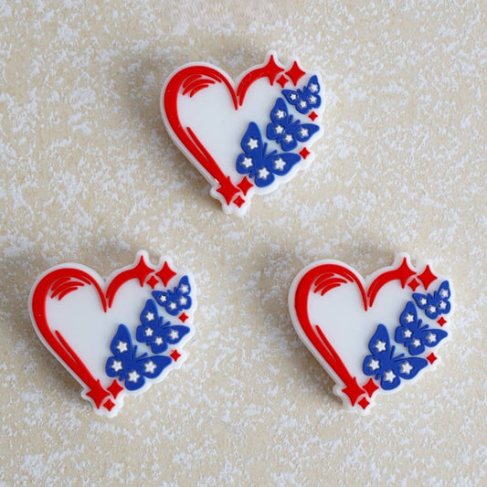 Three heart-shaped cookies with red, white, and blue butterfly designs on a textured beige background.


