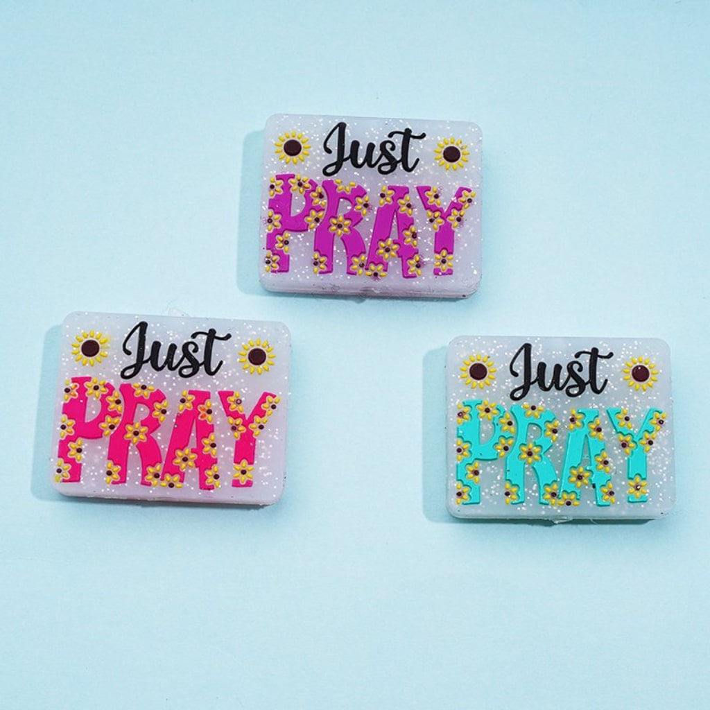 Three rectangular silicone beads with the phrase 'Just Pray' and a sunflower design in pink, blue, and green colors.

