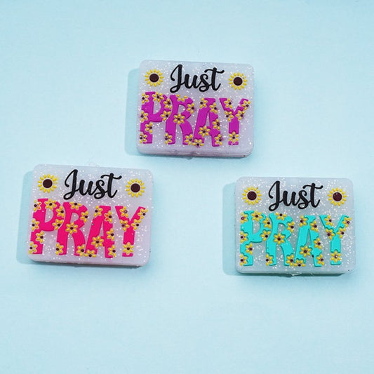 Three rectangular silicone beads with the phrase 'Just Pray' and a sunflower design in pink, blue, and green colors.

