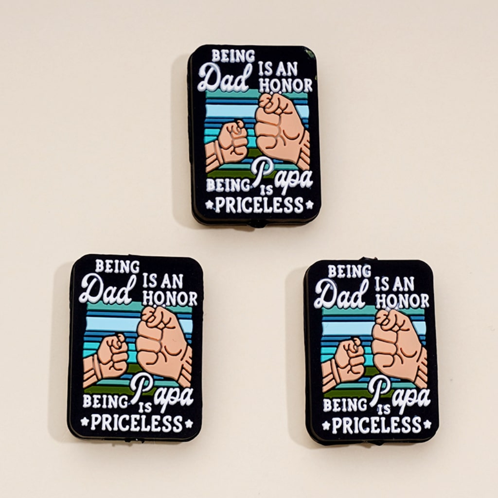 Three rectangular silicone beads with the message 'Being Dad is an Honor Being Papa is Priceless' printed on them, displayed against a white background.

