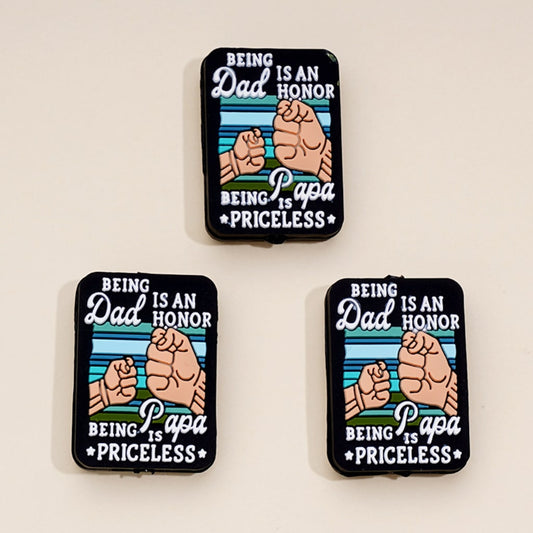 Three rectangular silicone beads with the message 'Being Dad is an Honor Being Papa is Priceless' printed on them, displayed against a white background.

