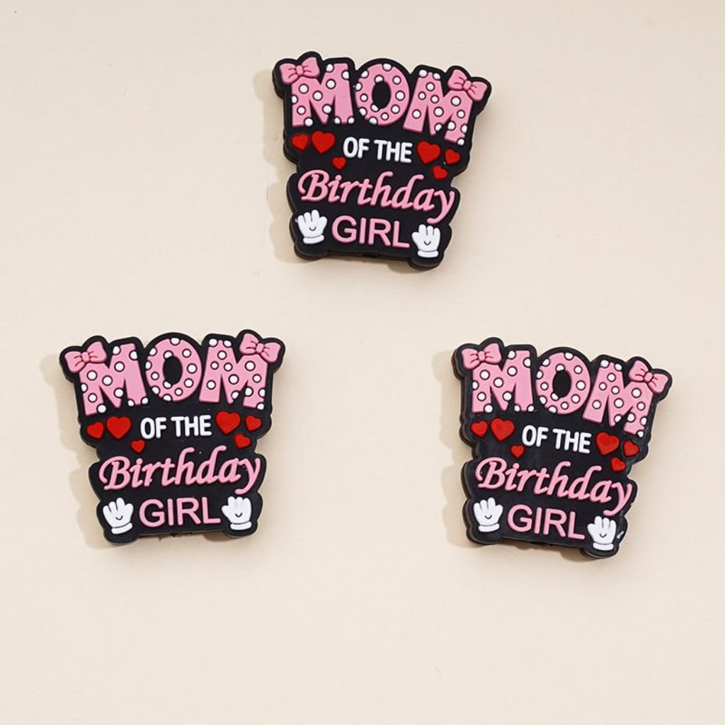 A set of three silicone beads with the text 'MOM OF THE BIRTHDAY GIRL' written on them, featuring pink bows and red hearts.

