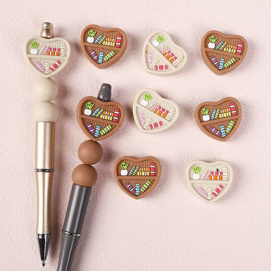 A collection of heart-shaped silicone beads in various colors, displayed alongside pens for scale.

