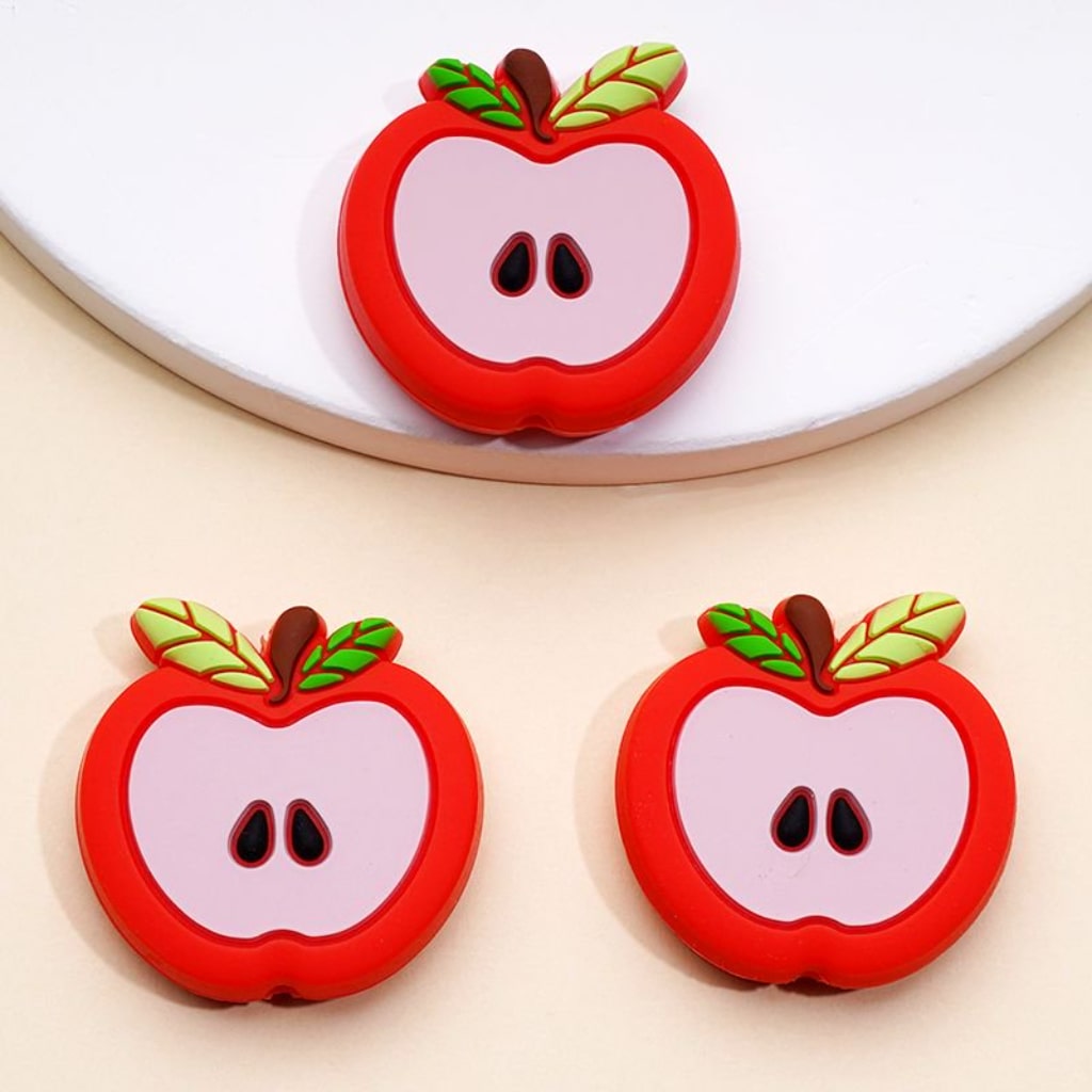 Three red silicone beads shaped like apples with leaves on a white background.

