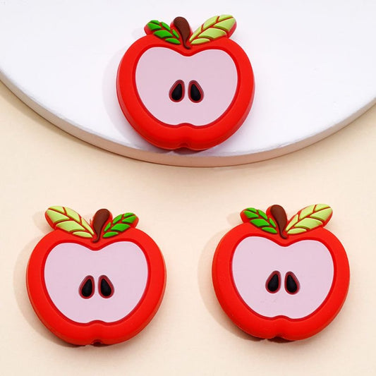 Three red silicone beads shaped like apples with leaves on a white background.

