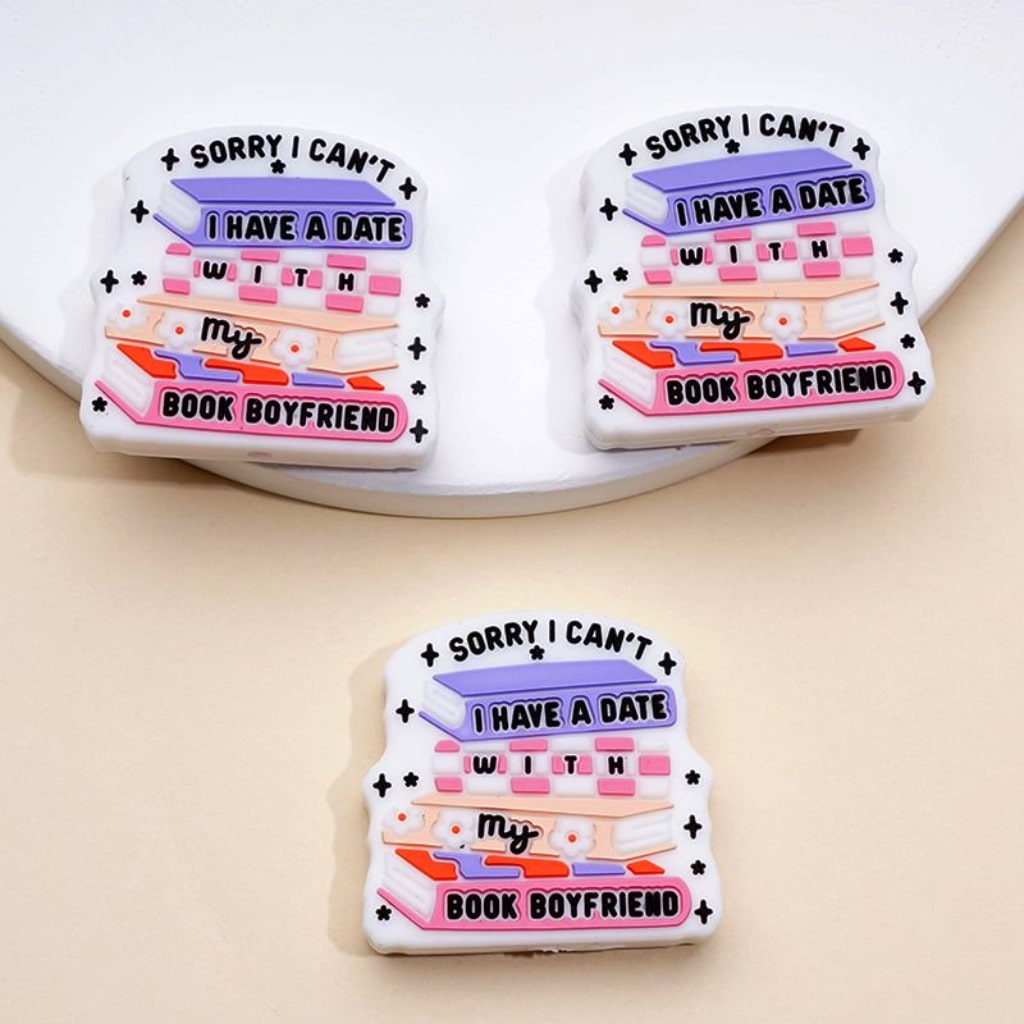 Three enamel pins with 'Sorry I can't, I have a date with my book boyfriend' text on a beige background.

