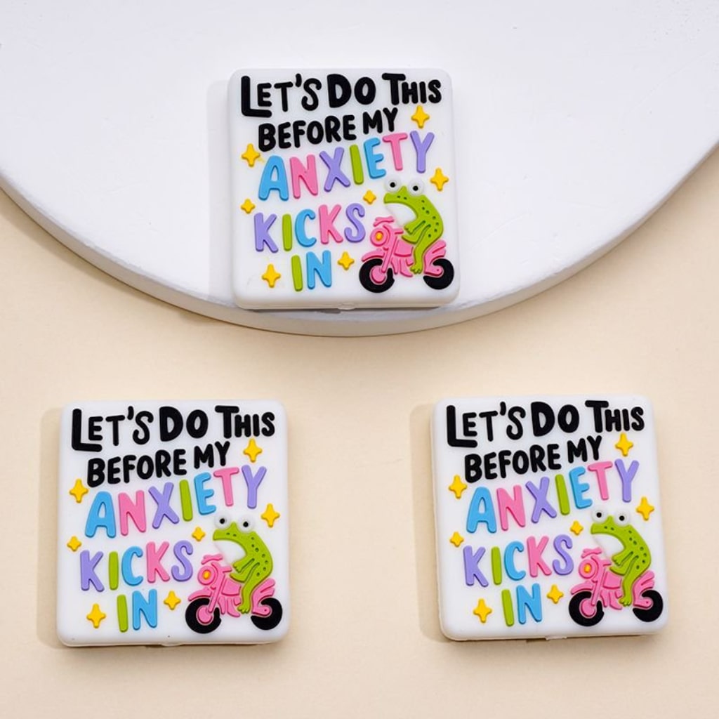 Three square silicone beads with the phrase 'Let's Do This Before My Anxiety Kicks In' and an illustration of a green frog riding a motorcycle.

