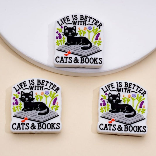 Silicone beads featuring a black cat sitting on a book with the phrase 'LIFE IS BETTER WITH CATS & BOOKS' printed above.

