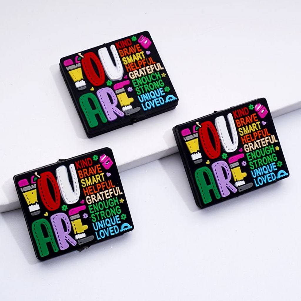 A set of rectangular silicone beads in various colors with text and形容词 printed on them, used for crafting.

