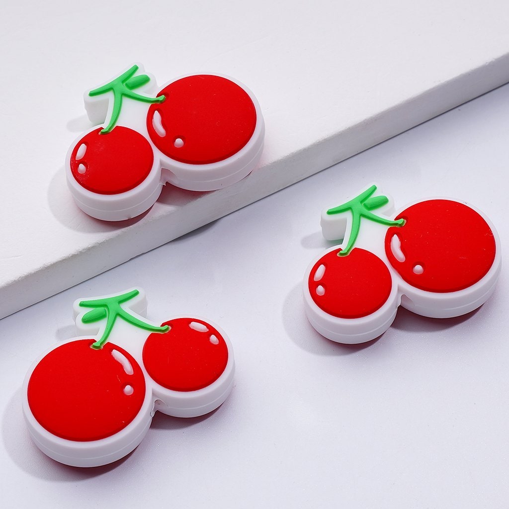 silicone beads designed to look like vibrant red cherries with white stems and green leaves, displayed on a white surface


