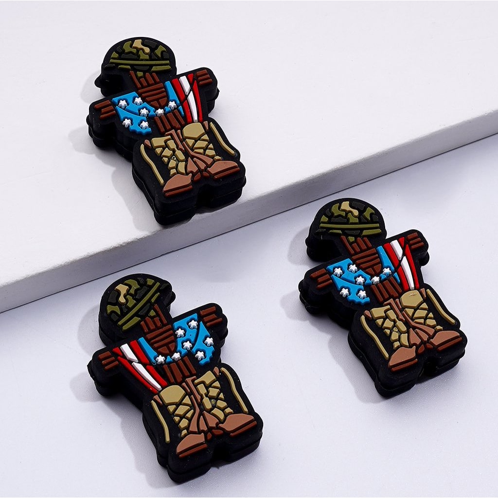 The image shows silicone beads in the shape of a soldier's tombstone, featuring a patriotic design with a camouflage pattern and the American flag.

