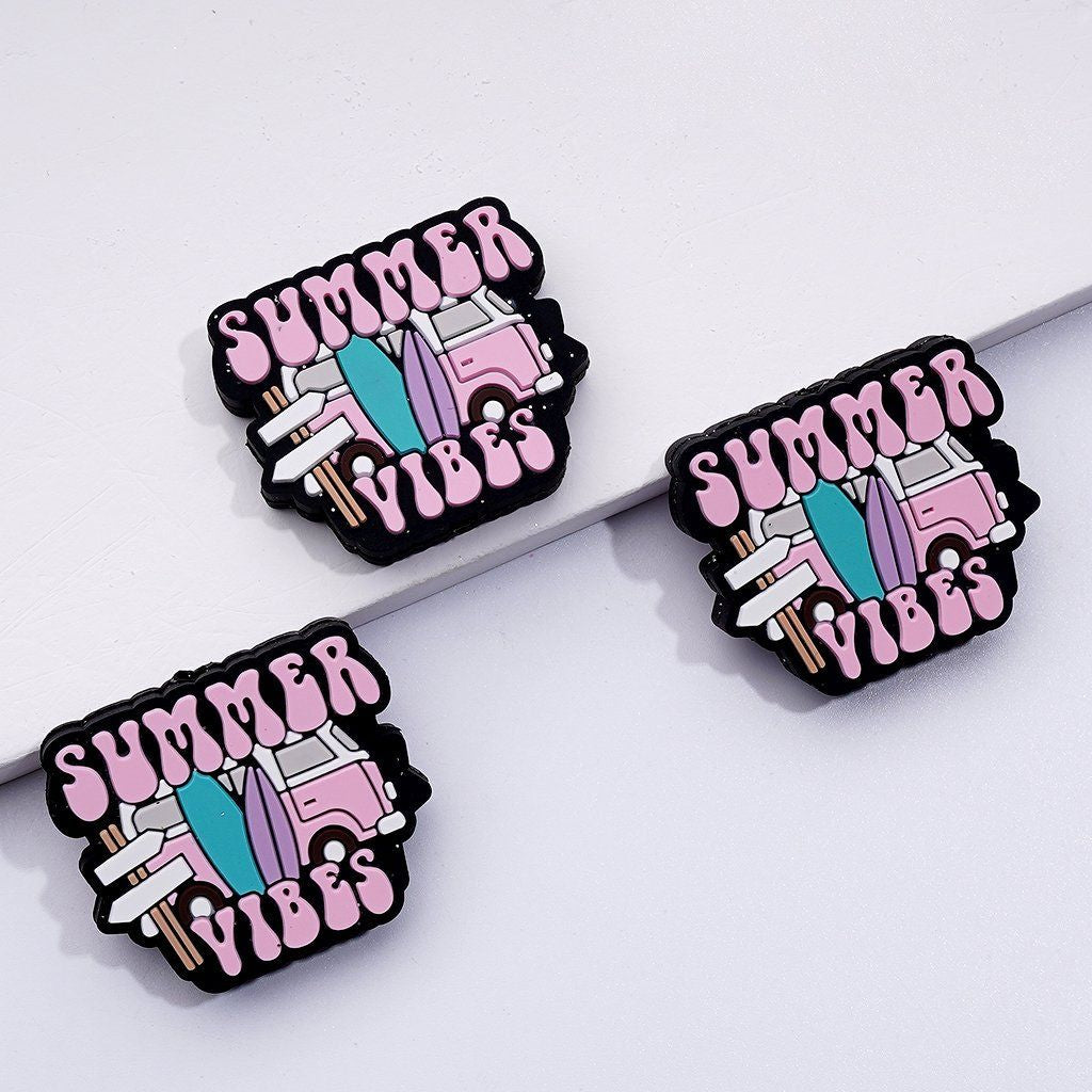 Three silicone beads with a summer van design and the text 'SUMMER VIBES' on them, predominantly pink with black and white details.

