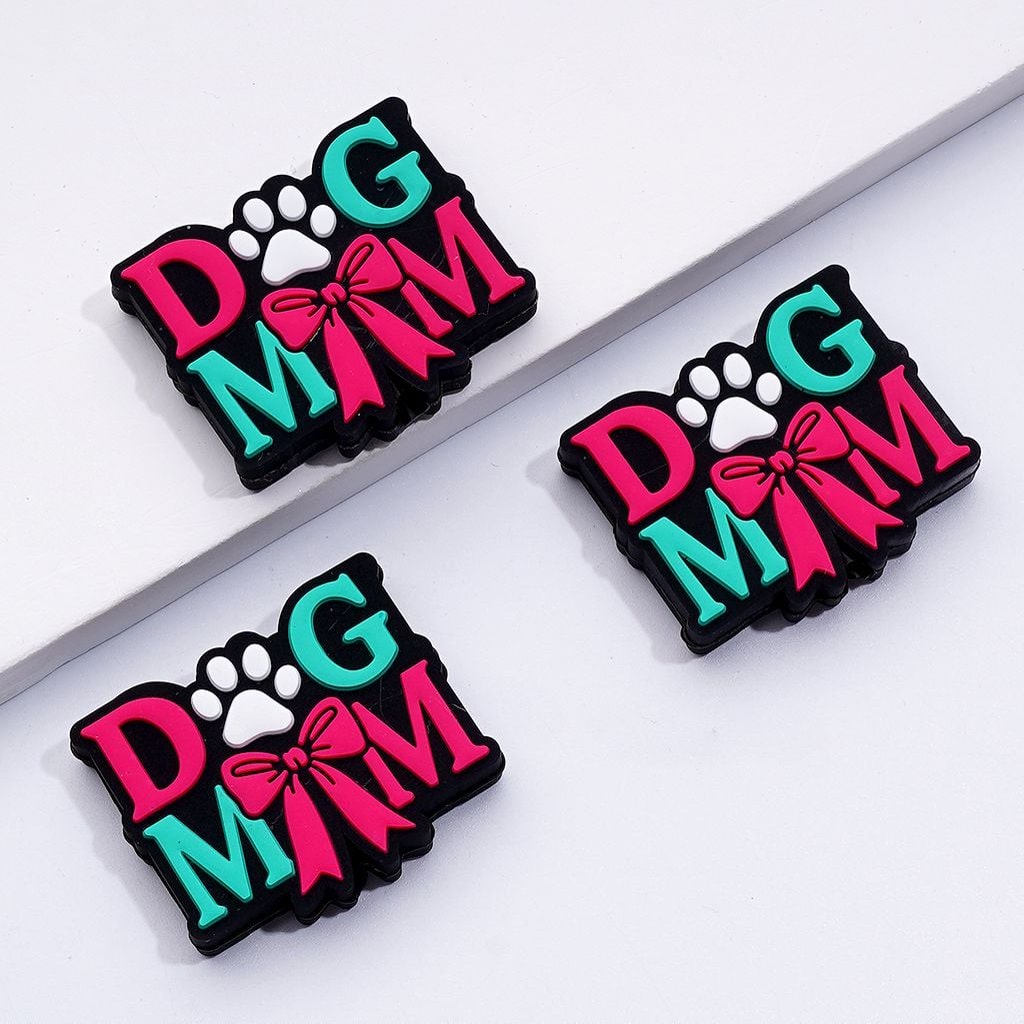 The image shows two silicone beads with the phrase 'DOG MOM' and cute paw prints, decorated with red and white colors and a red bowknot.

