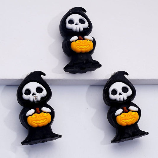 Three Halloween-themed earrings shaped like grim reapers holding pumpkins on a white background.

