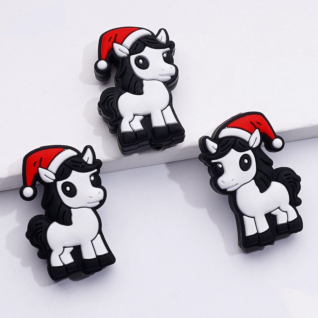 Three cartoon-style unicorn charms with Santa hats on a white background

