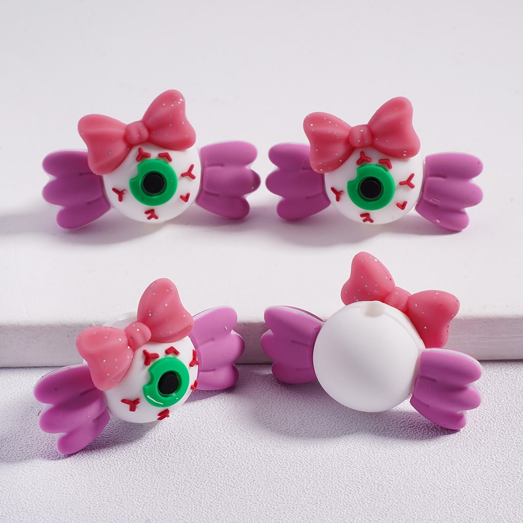 Three decorative beads with pink bows and green eyes on a white background

