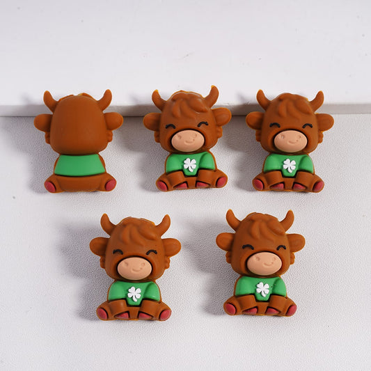 Five cartoonish cow figurines wearing green shirts with white clover patterns on a white background.

