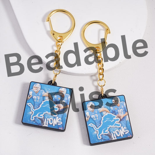 Pair of keychains with football players and 'Lions' logo on a white background