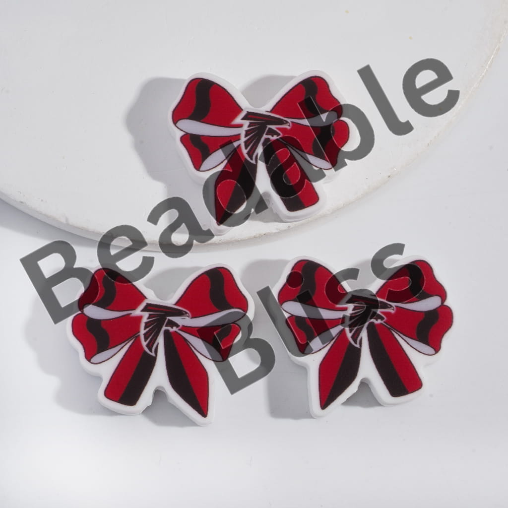 Red, black, and white bow-shaped earrings on a white background with 'handsontupply' branding.