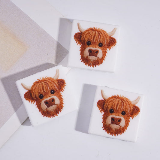 Three coasters with highland cow designs on a light gray background