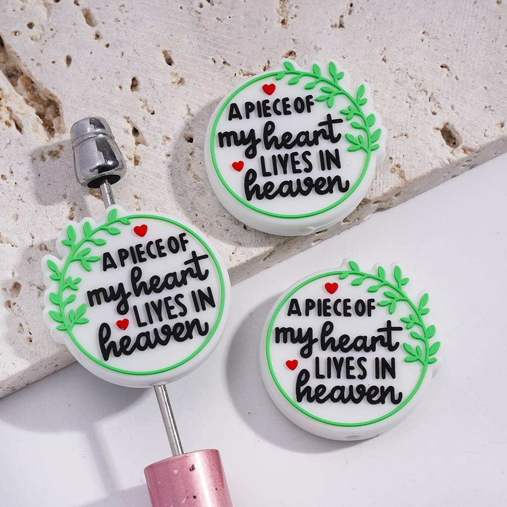 Three circular charms with 'A Piece of my heart lives in heaven' text on a textured surface.

