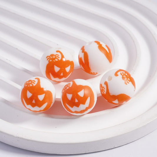 White and orange beads with pumpkin face designs on a white plate.

