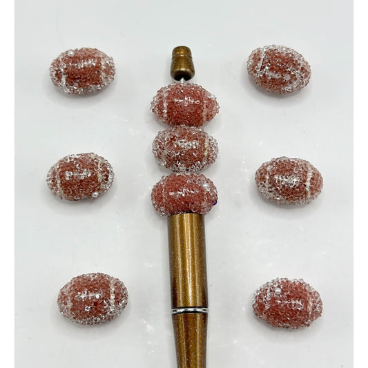 Acrylic beads in brown color with a design resembling a football, displayed alongside a tool for crafting.

