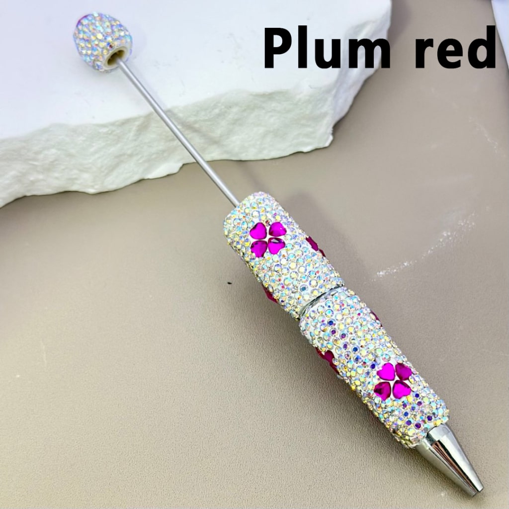 Decorative pen with gemstones and plum red accents on a beige surface