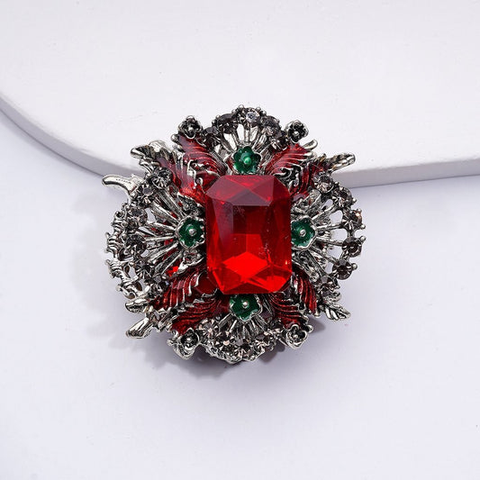 Decorative brooch with a red gemstone and silver metalwork on a white background


