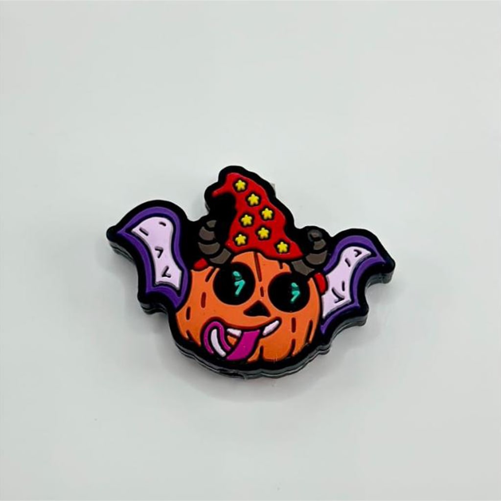A silicone bead featuring a design with purple wings and a character resembling a pumpkin with eyes and a tongue sticking out, topped with a red star hat.

