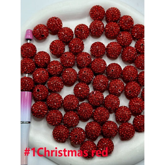 A collection of round clay beads, featuring red and green colors with white rhinestones, arranged on a plate with a pen for scale.

