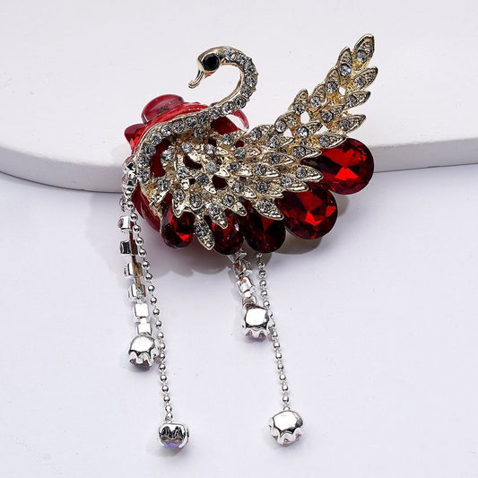 Decorative brooch with swan design and gemstones on a white background

